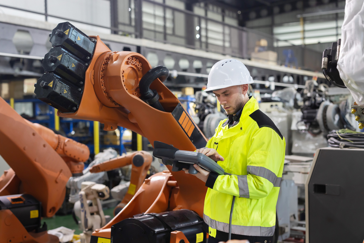Engineer using a digital tablet to inspect robotic machinery on an automated manufacturing production line.